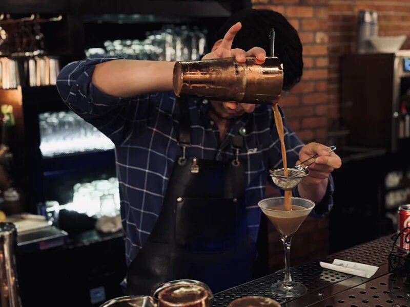 Bartender straining a cocktail through a fine mesh at the cantina bar